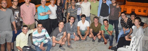 A group of people gathered in an outdoor setting with a stone wall and a building in the background.