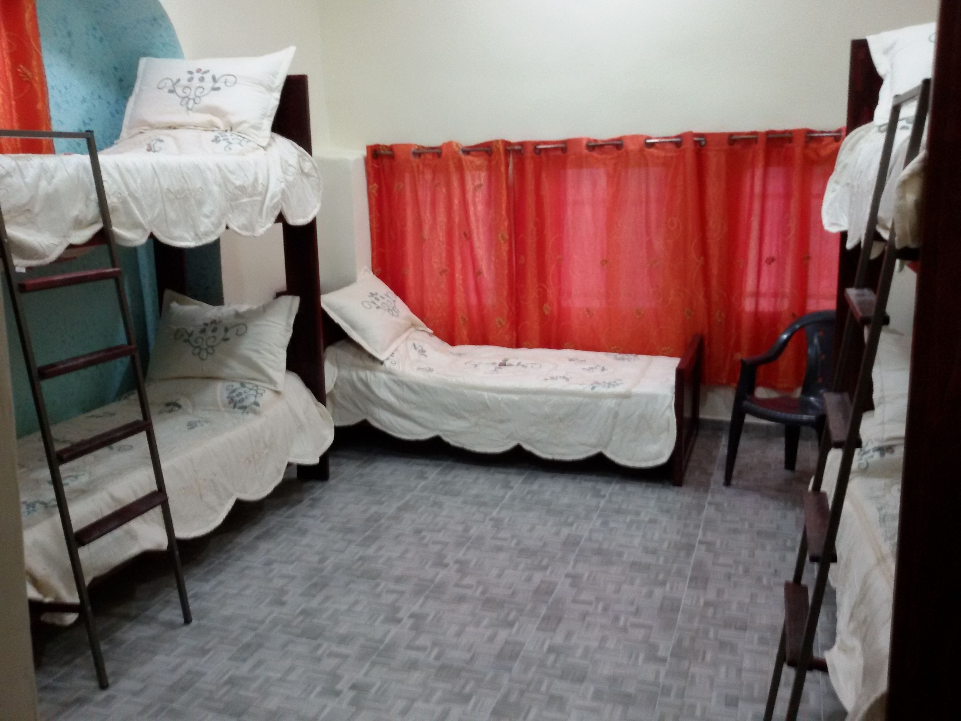 A dormitory room with bunk beds, a chair, and a curtain.