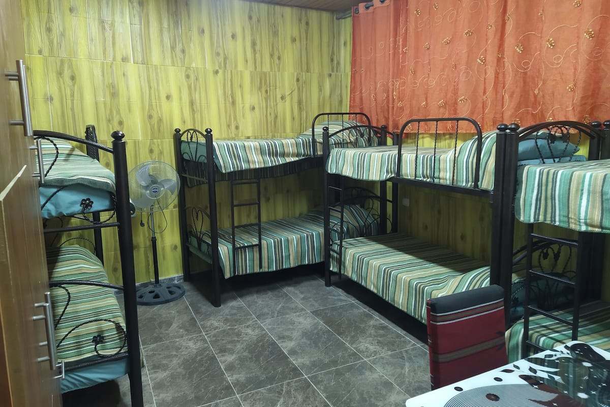 A dormitory room with bunk beds, a fan, and a small table.