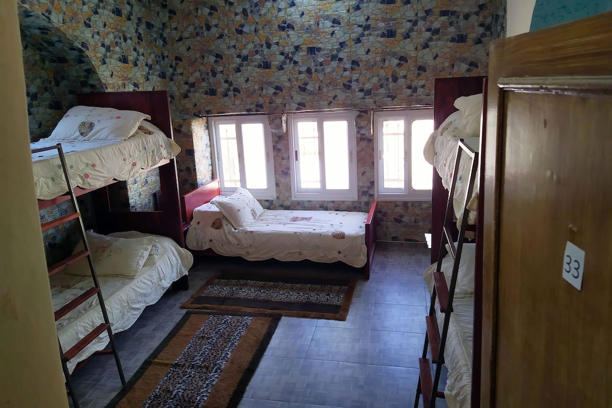 A dormitory room with bunk beds, a wooden wardrobe, and a window with a view.