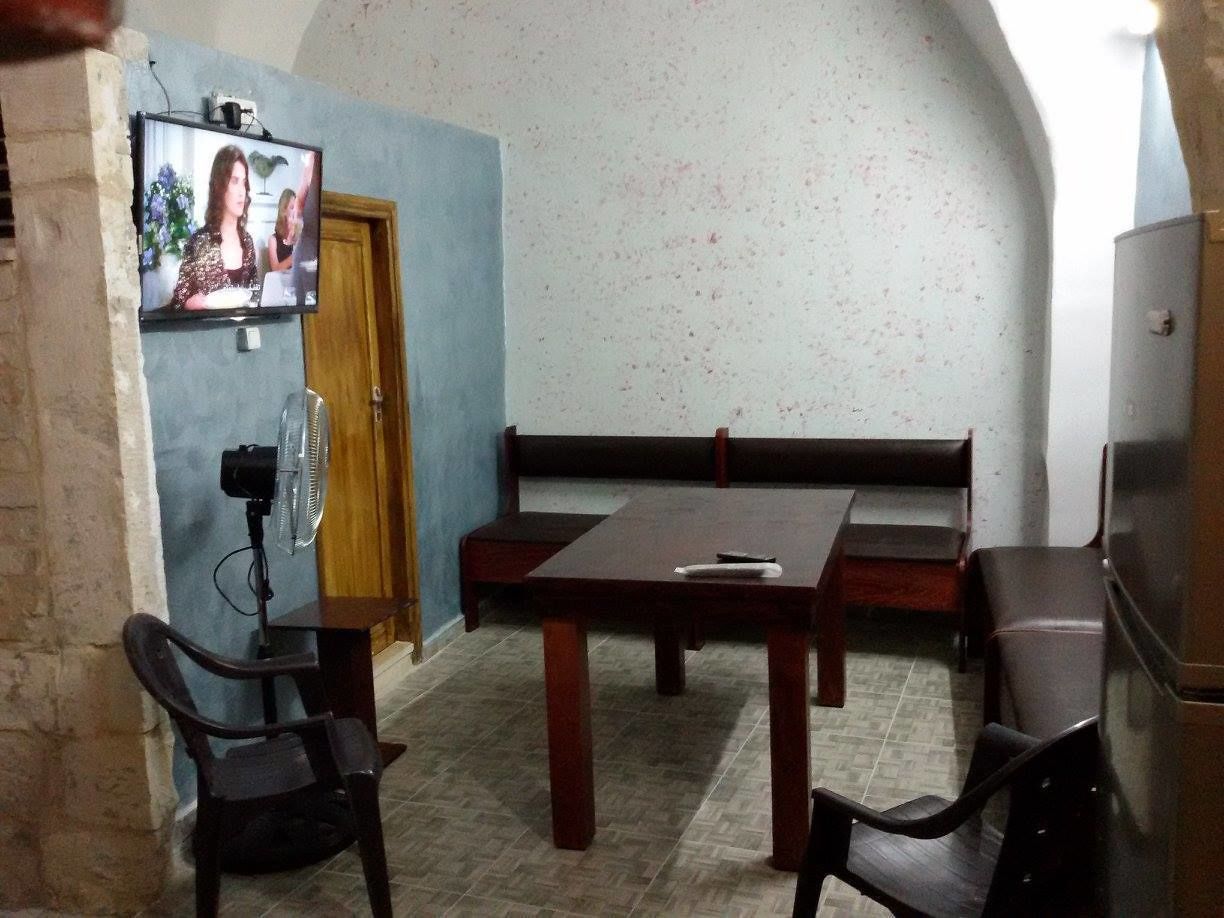 Un coin repas comprenant une table en bois, quatre chaises, un banc, un téléviseur et un ventilateur.