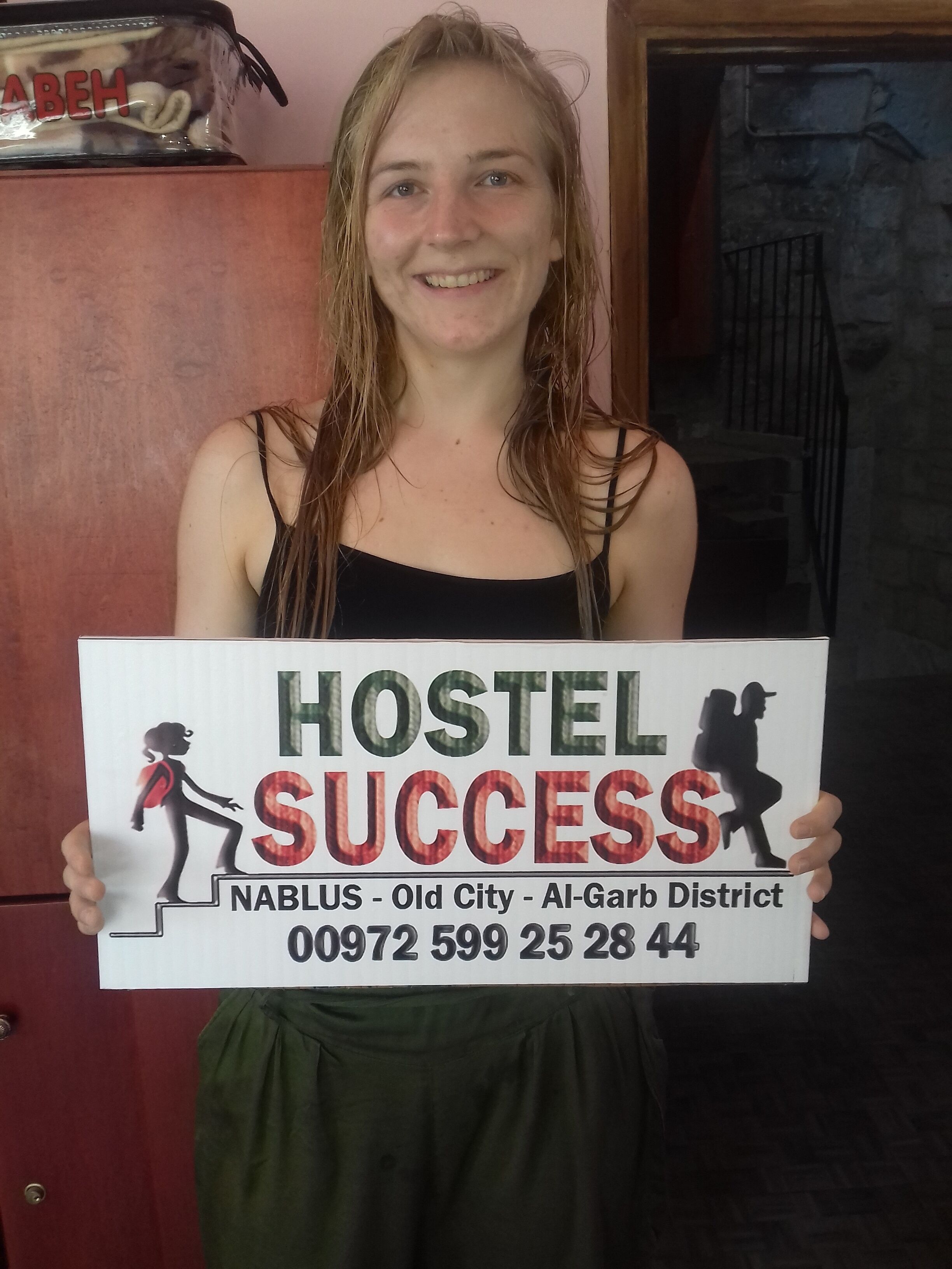 A person holding a sign that reads "HOSTEL SUCCESS" with a silhouette of a person climbing steps.