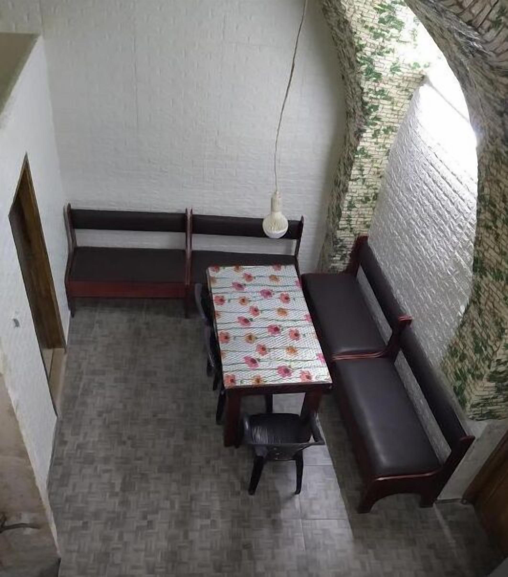 A small, enclosed dining area with a table and benches, a hanging light fixture, and a brick wall.