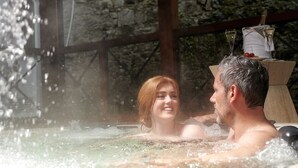 A couple in a hot tub with a stone wall and a wooden structure in the background. - Dromoland Castle (Newmarket on Fergus)