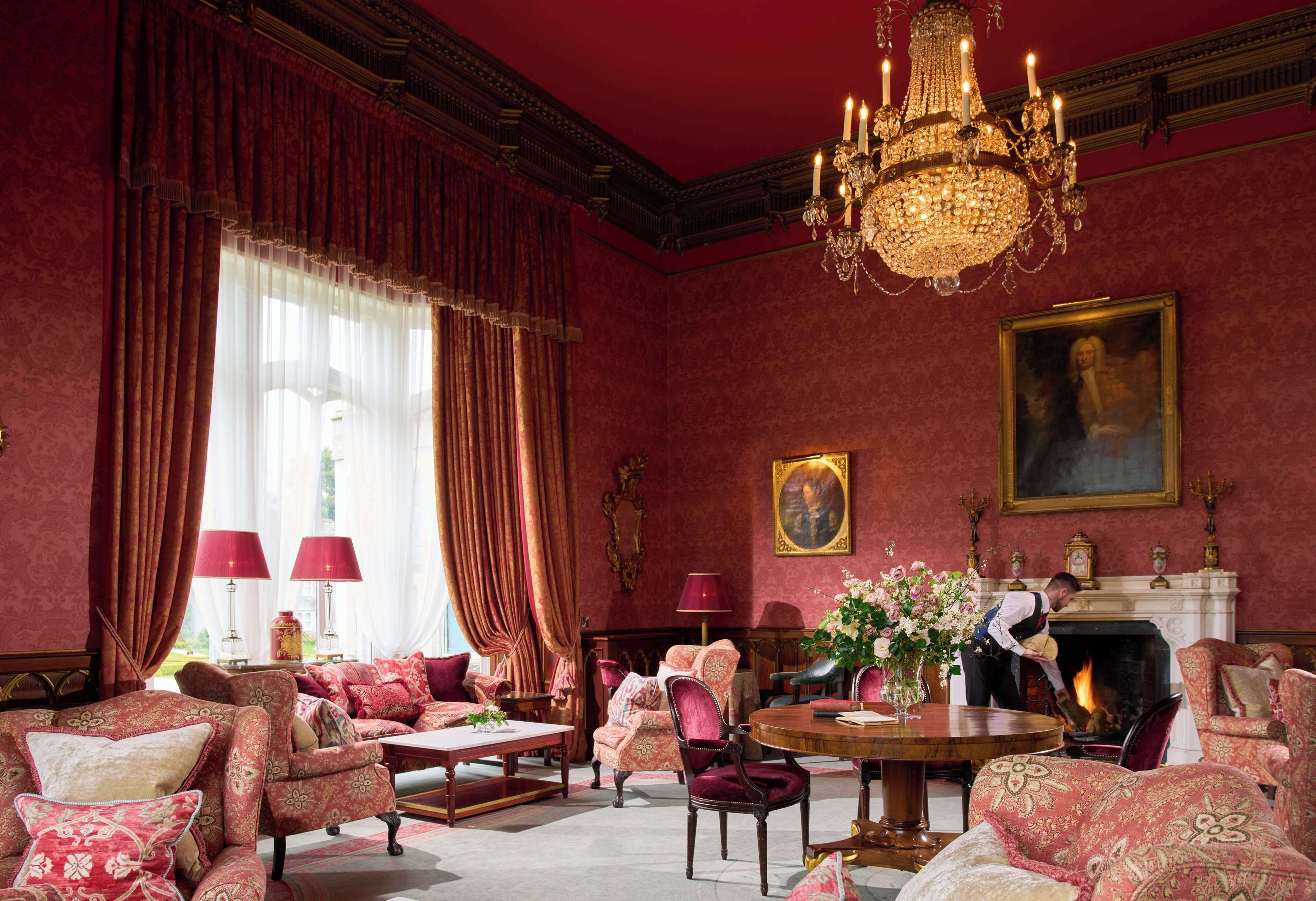 A richly decorated room with red walls, ornate furniture, and a large chandelier.