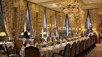 Una larga mesa de comedor dispuesta para una comida formal, con múltiples candelabros y cortinas drapeadas.