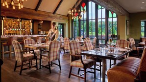 A restaurant with a bar area, large windows, and plaid chairs. - Dromoland Castle (Newmarket on Fergus)