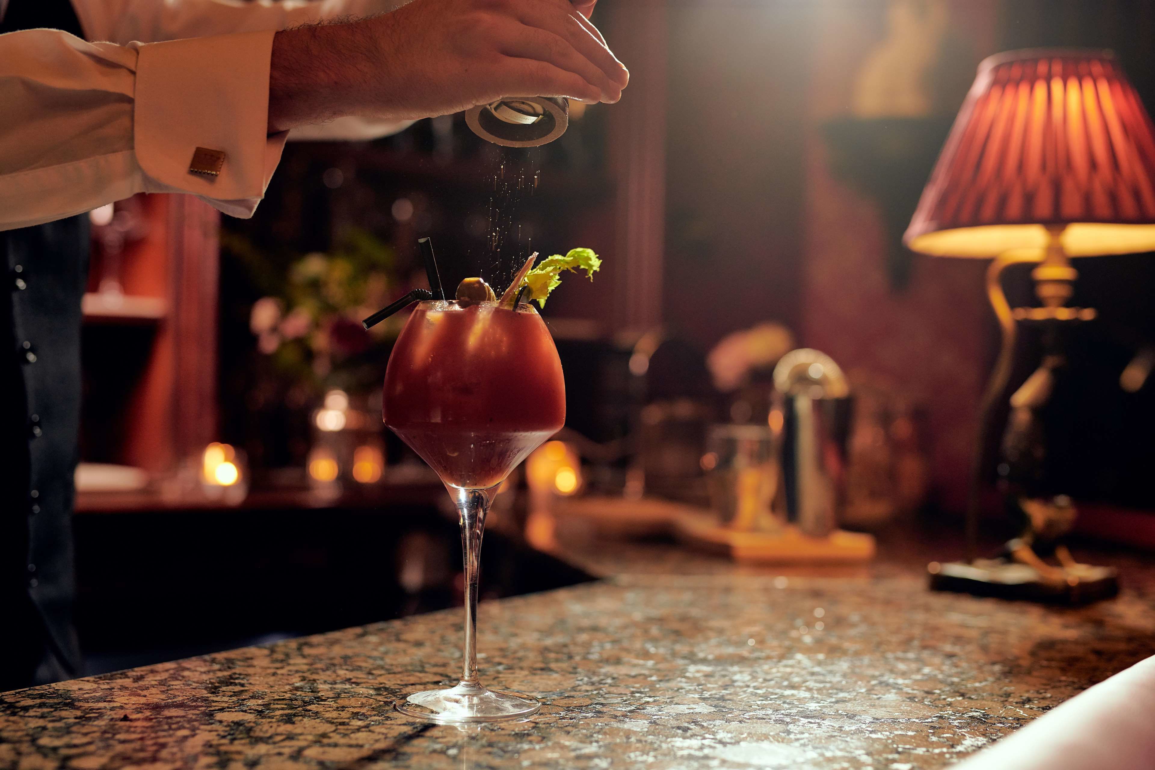Une personne verse une boisson dans un verre, et un élément de décoration est posé sur le comptoir du bar.