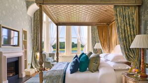 A luxurious bedroom with a large bed, a fireplace, a television, and a view of a lake. - Dromoland Castle (Newmarket on Fergus)