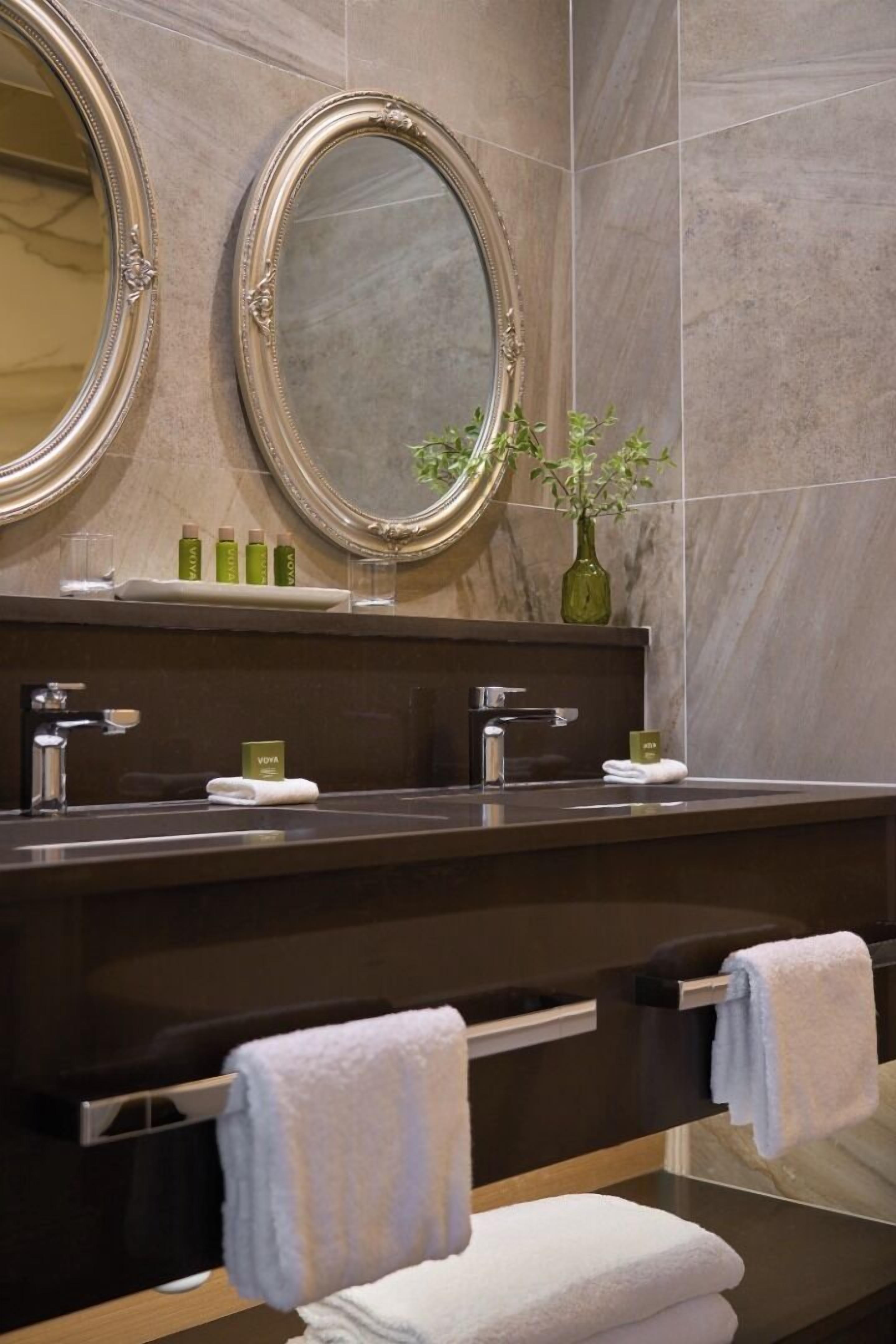 A bathroom with two mirrors, a sink, and a towel rack.