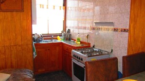 A compact kitchen with wooden cabinets, a gas stove, and a window providing natural light. - Ventanas del Lago (Puerto Varas)