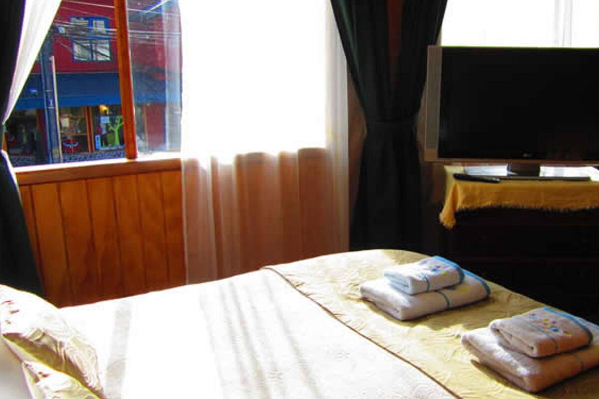 A hotel room with a bed, a television, and a window with curtains.