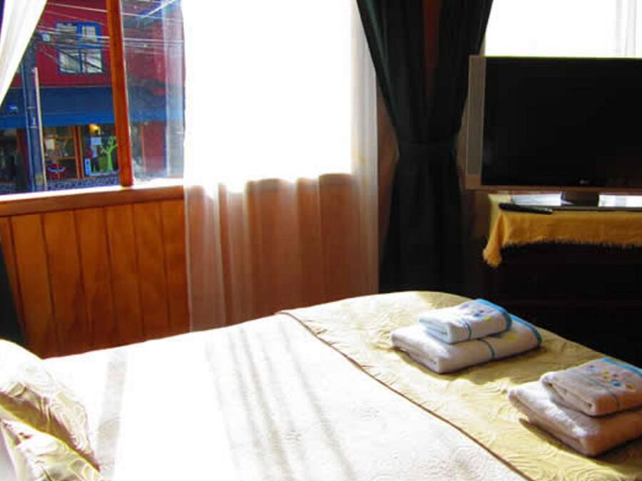A hotel room with a bed, a television, and a window with curtains.
