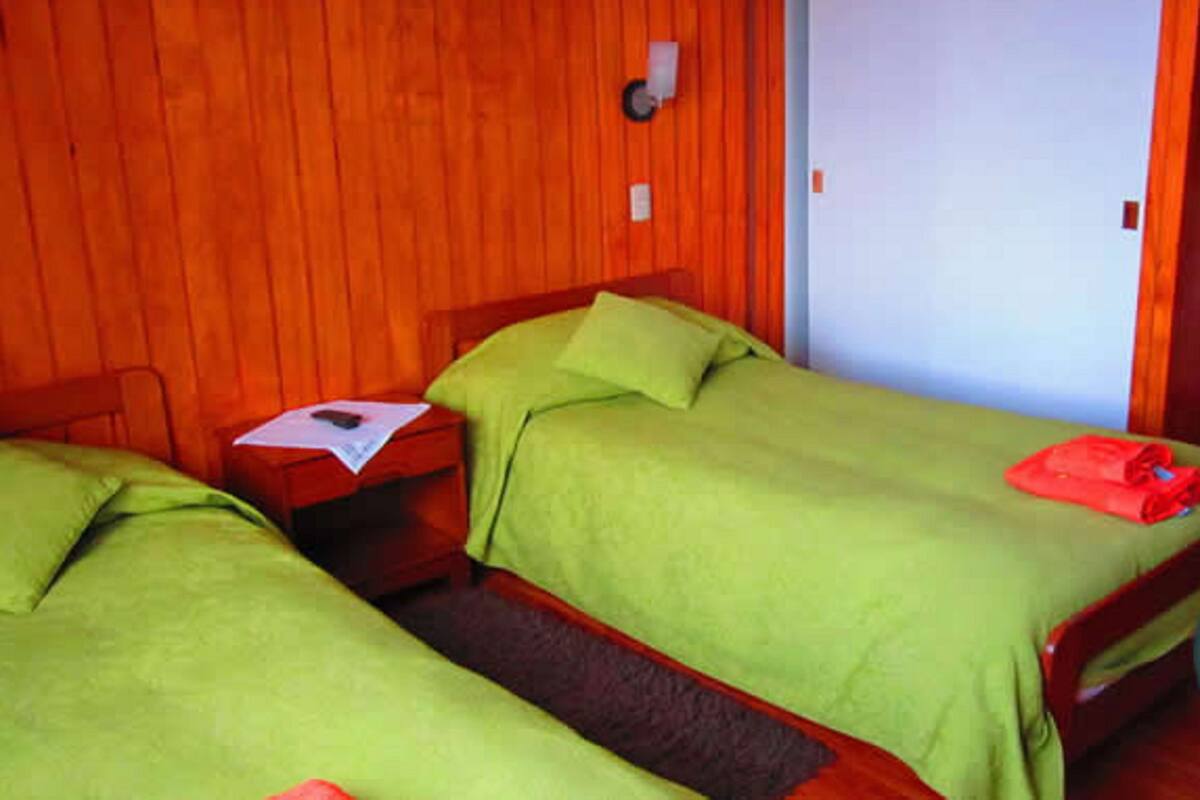 A room with two single beds, wooden walls, a small bedside table, and a door.