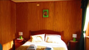 A wooden-paneled room with a bed, two nightstands, and a framed picture on the wall. - Ventanas del Lago (Puerto Varas)