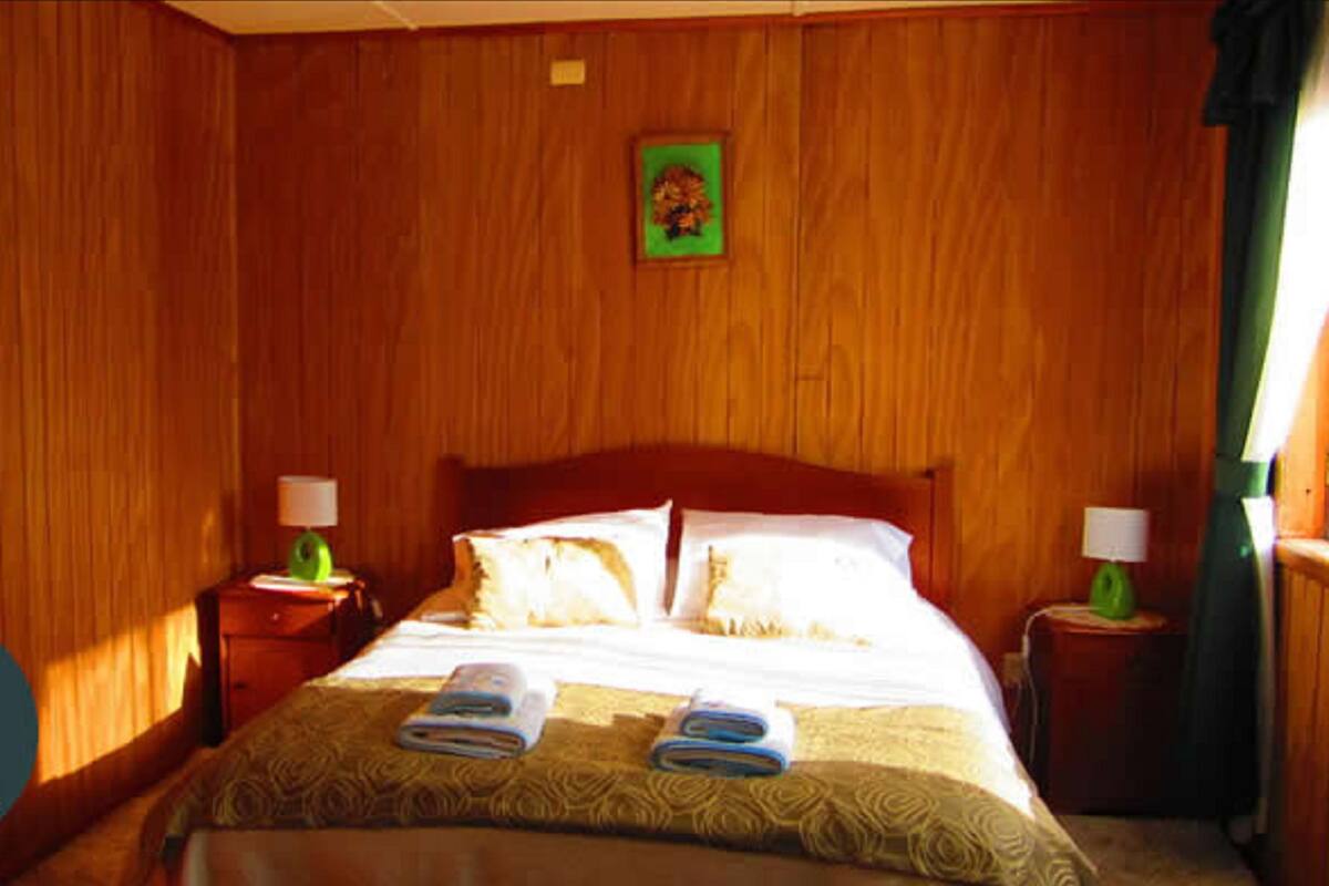 A wooden-paneled room with a bed, two nightstands, and a framed picture on the wall.