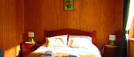 A wooden-paneled room with a bed, two nightstands, and a framed picture on the wall.