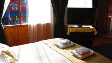 A hotel room with a bed, a television on a stand, and a window with curtains.