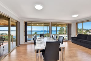 Een moderne eetruimte met een tafel voor zes personen, grote ramen met uitzicht op zee, en een balkon met een houten terras.
