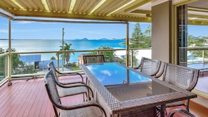 Un balcon avec une table en verre et des chaises en osier, offrant une vue sur la côte.