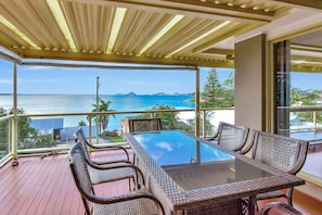 Een balkon met een glazen tafel en rieten stoelen, met uitzicht op de kust.