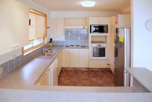 A compact kitchen with a sink, stove, microwave, oven, and refrigerator. - Seaside Serenity Soldiers Point (Soldiers Point)