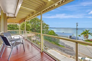 A wooden deck with chairs, a view of the ocean, and a road with vehicles. - Seaside Serenity Soldiers Point (Soldiers Point)
