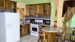 A kitchen with wooden cabinets, a white refrigerator, a stove, and a dining area with a round table and chairs. - Book now and u can save 20%OFF JUNE JULY 
FOR EARLY BIRD SALE IN SUMMER BOOKING  (Ochio Rios)