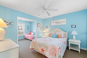 Une chambre à coucher comprenant un lit, une table de chevet, une chaise, un ventilateur de plafond et une fenêtre avec des stores.