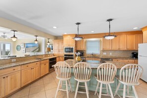 A kitchen with wooden cabinets, granite countertops, a central island with bar stools, and modern appliances. - Majak Moments: Exceptionally spacious oceanfront 7BR home in Holden Beach. (Holden Beach)
