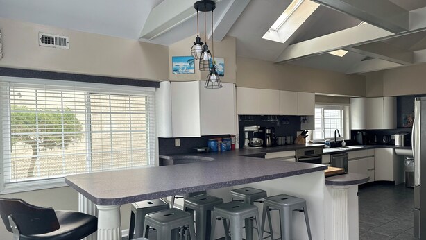 A modern kitchen with a central island, bar stools, and a window with blinds.