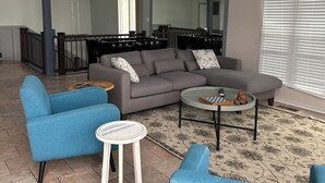 A modern living room with a grey sectional sofa, blue armchairs, a small white table, and a patterned rug.