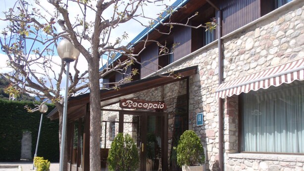A stone building with a sign reading "Recepció" and a "H" indicating a hotel. There are potted plants in front of the entrance. - Hotel La Seu (La Seu d'Urgell)