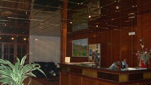 A reception area with a wooden reception desk, a painting on the wall, and a potted plant. - Hotel La Seu (La Seu d'Urgell)
