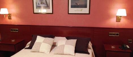 Quarto de hotel com uma cama grande, duas mesas de cabeceira e duas luminárias fixadas na parede.