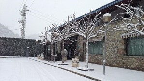 A snow-covered building with a stone facade, a paved driveway, and bare trees. - Hotel La Seu (La Seu d'Urgell)