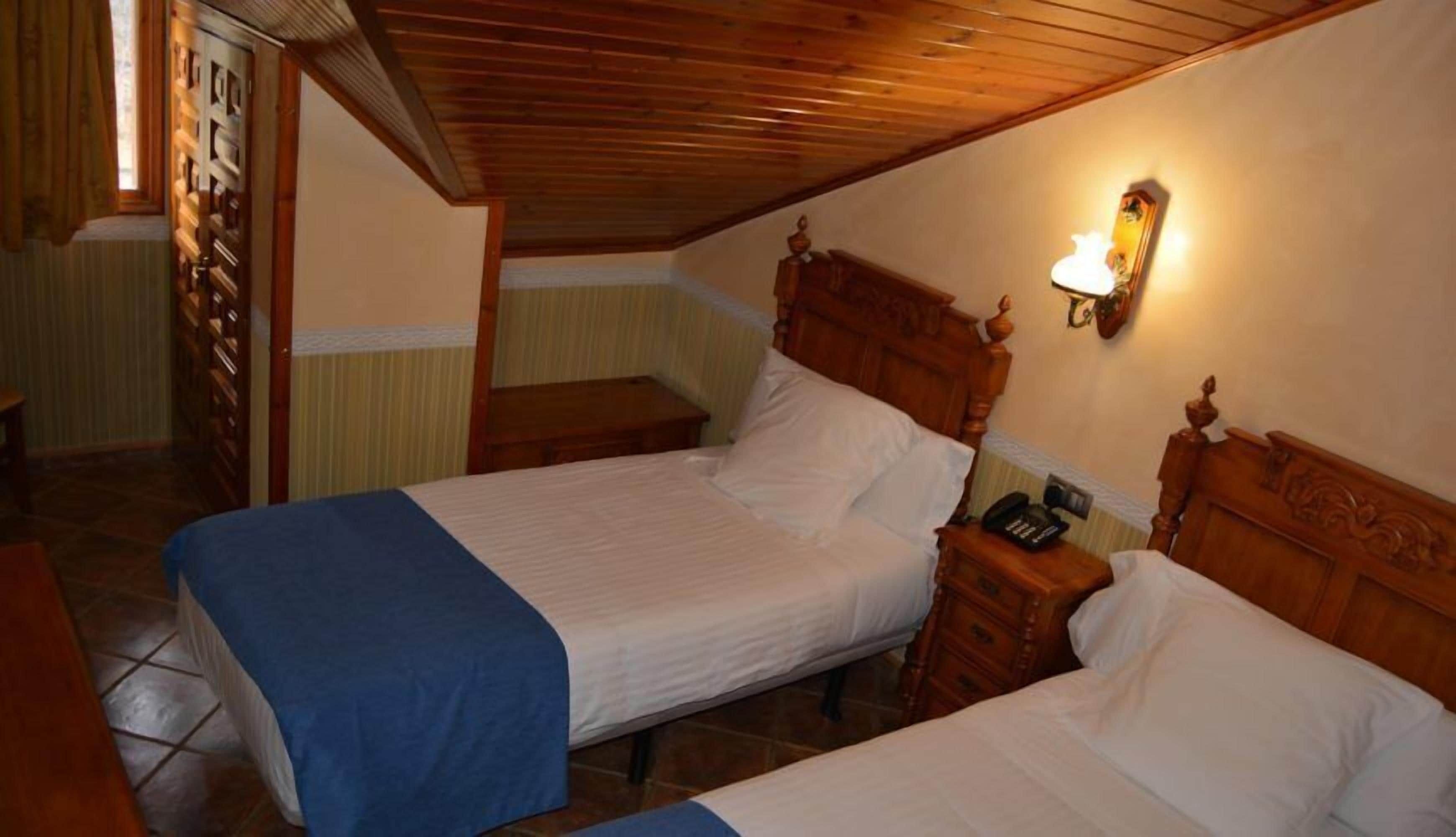 Un dormitorio con dos camas, cabeceros de madera, una mesita de noche con lámpara y techo de madera.