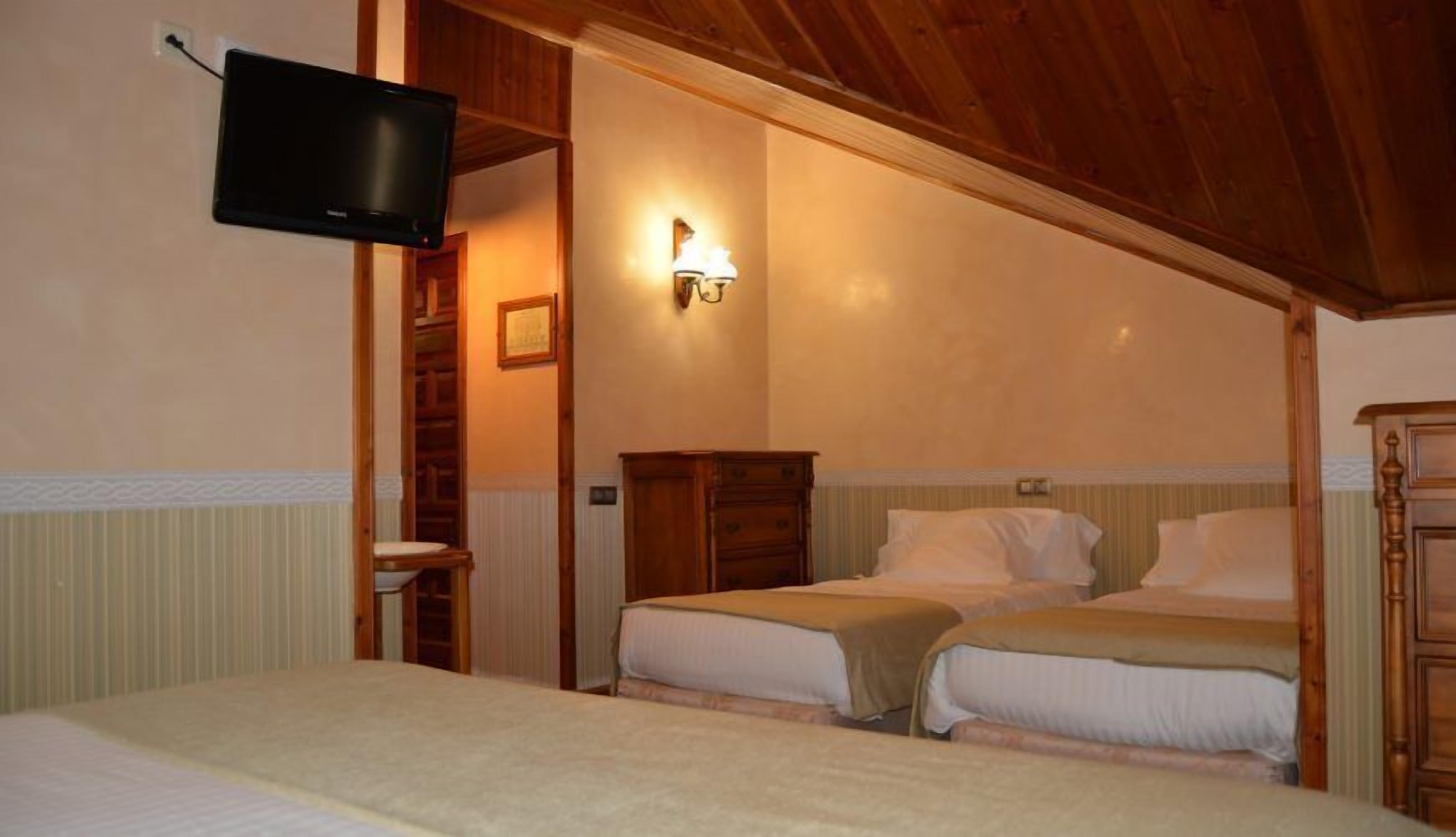 Un dormitorio con dos camas, una televisión instalada en la pared y un armario de madera.