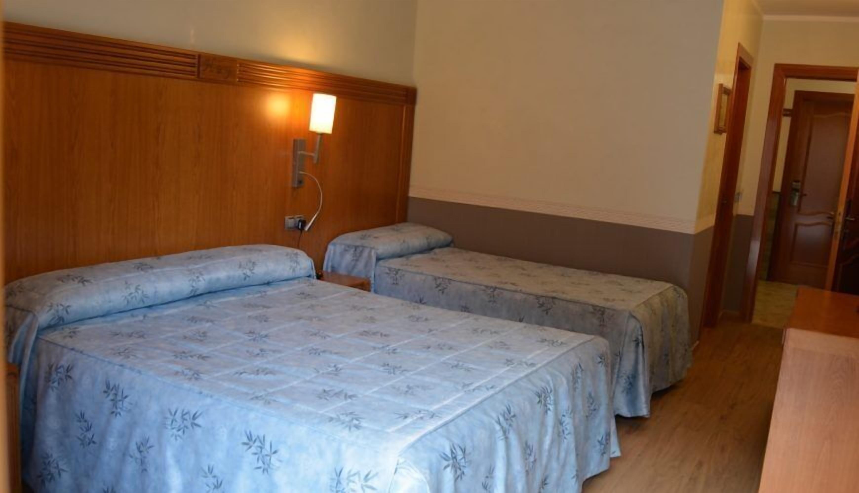 Une chambre d’hôtel avec deux lits, une tête de lit en bois, une petite lampe de chevet et une porte donnant sur une autre pièce.