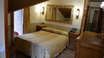 A bedroom with a large bed, a wooden dresser, a nightstand with a phone, and a mirror above the bed.
