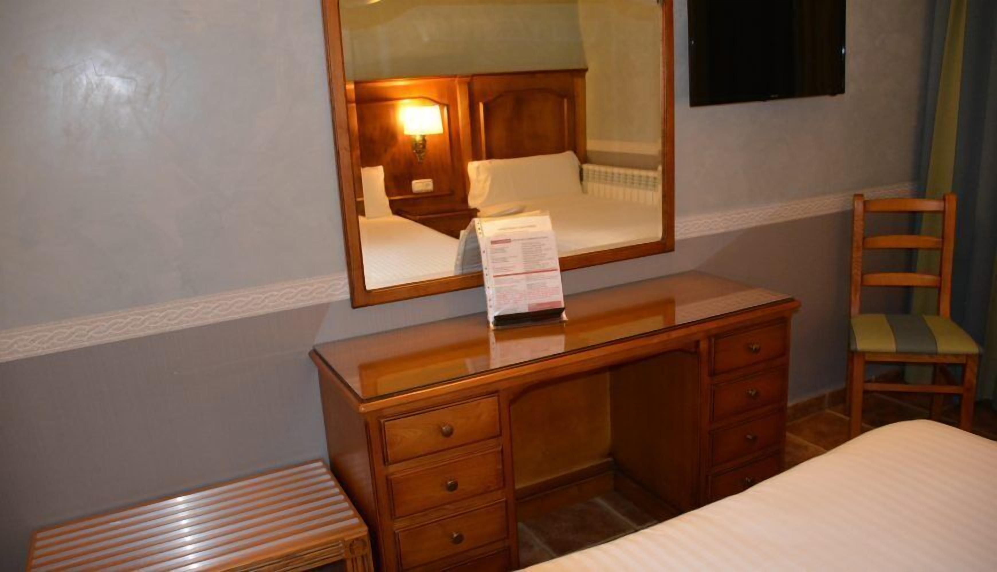 A hotel room with a wooden desk, a mirror, a chair, and a bed.