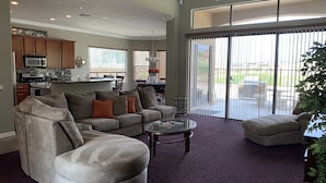Ein geräumiges Wohnzimmer mit einem grauen Ecksofa, einem Glastisch und einer großen Schiebetür, die auf eine Terrasse führt.