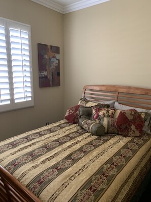 A bedroom with a wooden bed, patterned bedding, a window with blinds, and a painting on the wall.