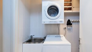 A compact laundry room with a front-loading washing machine, a sink, and a built-in dryer.
