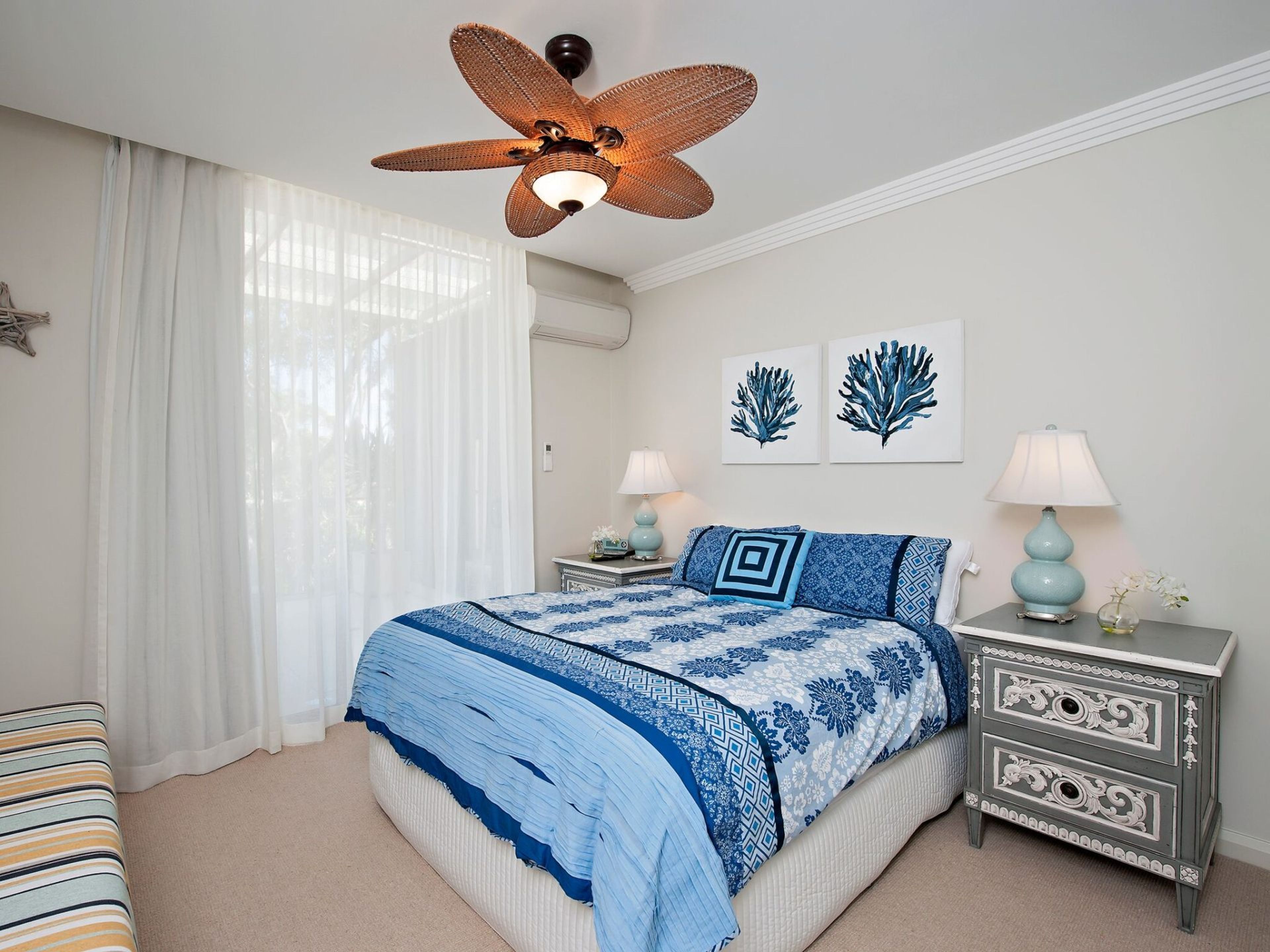 A bedroom with a bed, two bedside tables, a ceiling fan, and artwork on the wall.