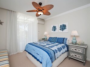 A bedroom with a bed, two bedside tables, a ceiling fan, and artwork on the wall.