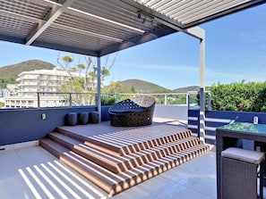 A covered outdoor area with steps leading to a seating area, a table, and a view of a hillside. - Aura Apartments U12 Shoal Bay Beach Views (Shoal Bay)