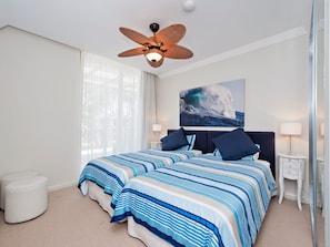 Een slaapkamer met een groot bed, een plafondventilator, een schilderij van een golf en een nachtkastje met een lamp.