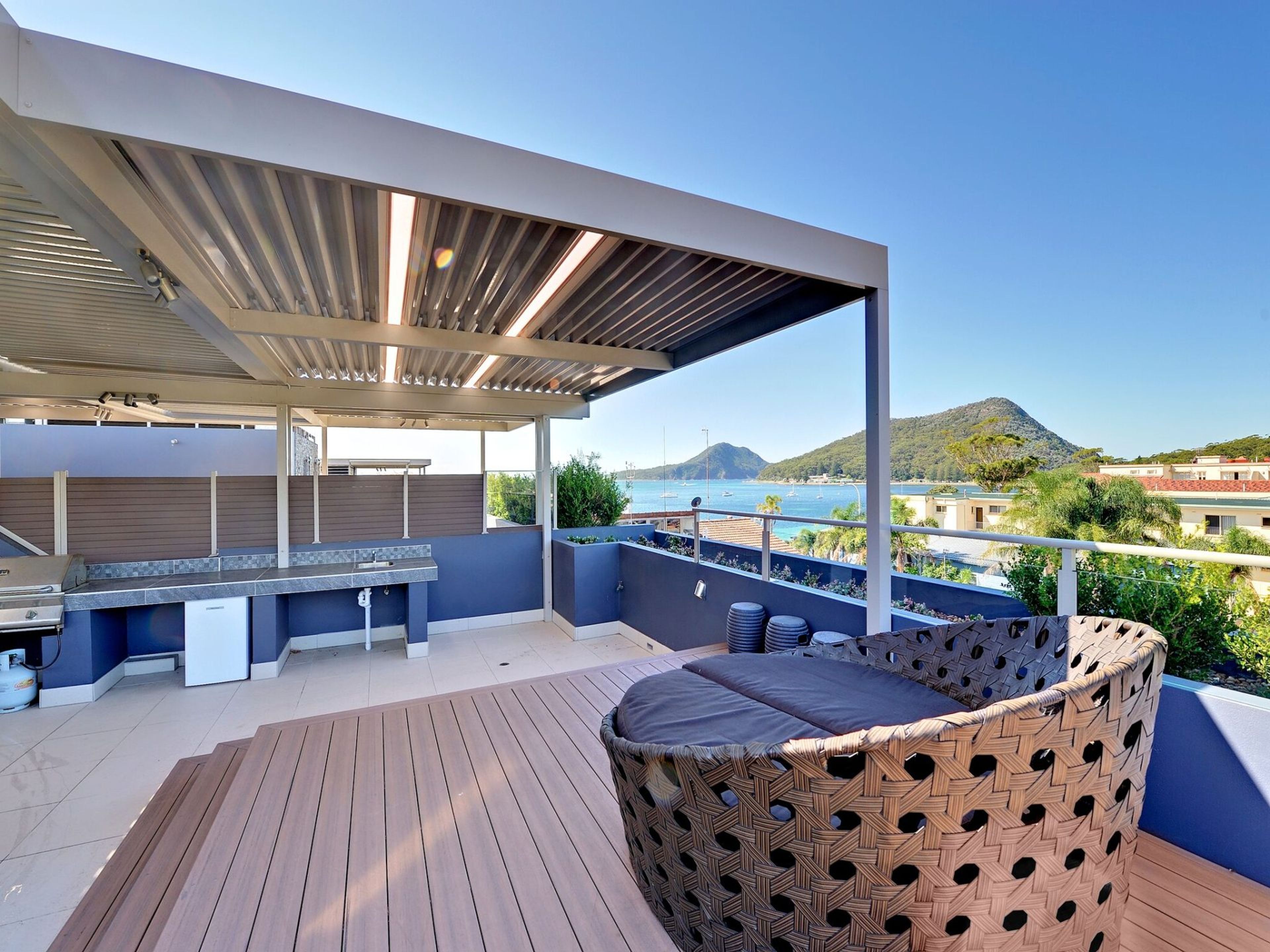 A covered outdoor area with a barbecue, seating, and a view of the sea.
