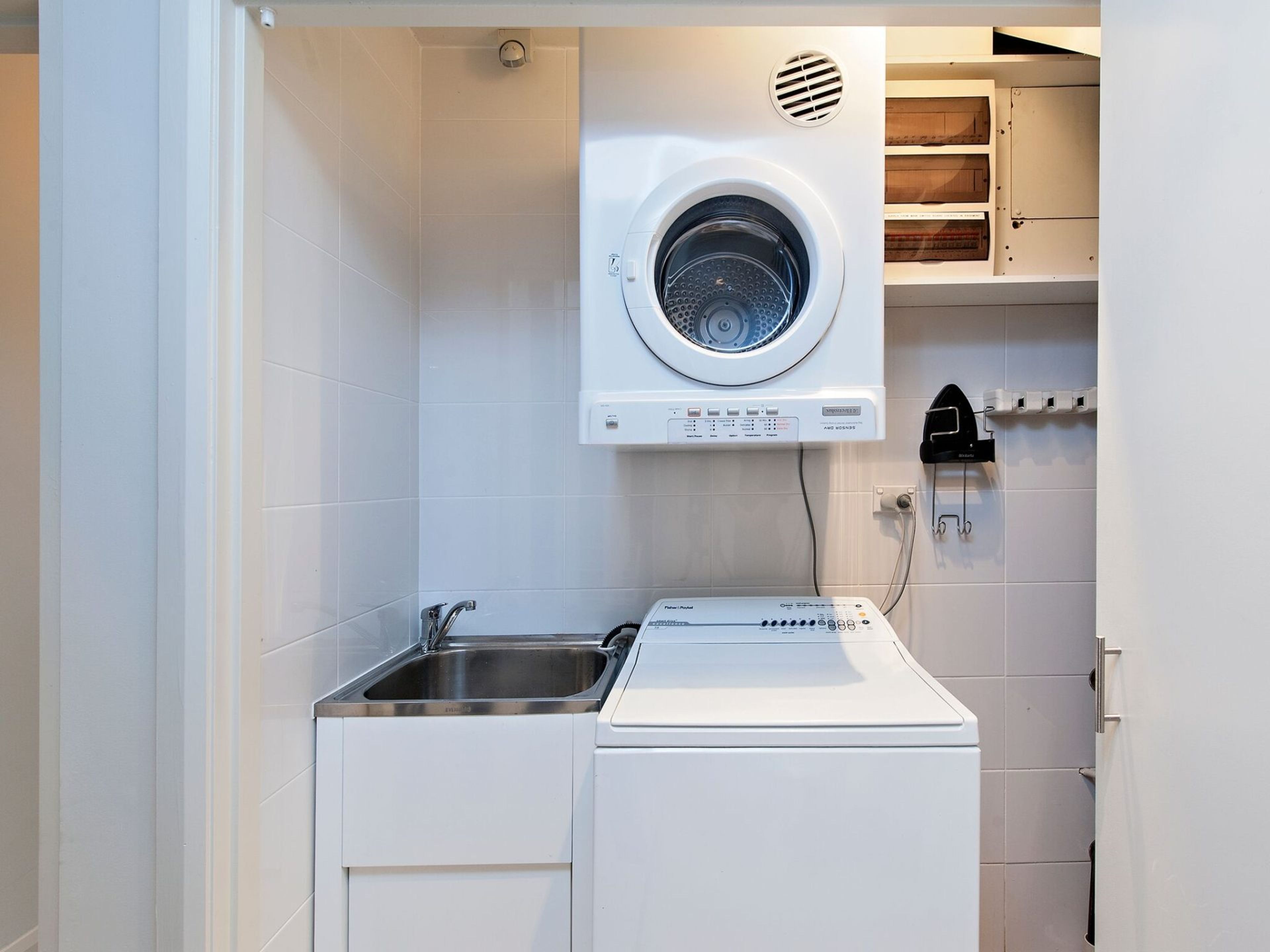 A compact laundry room with a front-loading washer and dryer, a sink, and a wall-mounted heater.